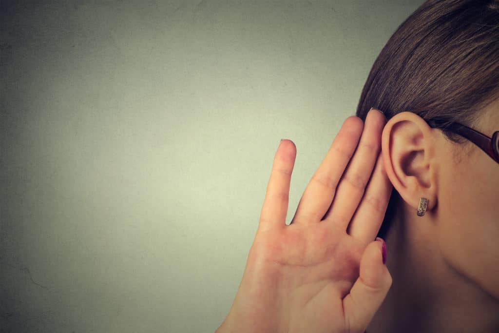 Woman placing hand behind ear gesticulating to hear